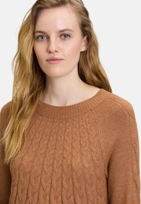 Brauner, kabelgestrickter Pullover mit weiter Ausschnitt, der texturierte Muster und gerippte Akzente am Kragen aufweist. Weiches, mittelschweres Material.