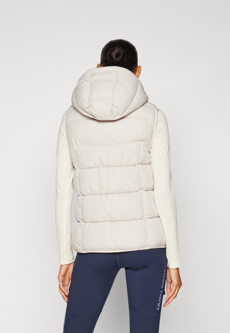 Beige gewatteerde vest met een grote capuchon, voorzien van horizontale stikdetails, een gladde textuur en een getailleerd silhouette. Gekleed over een lichte top.