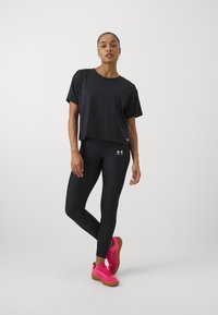 Svart avkortet t-skjorte, svarte leggings og lyse rosa treningssko. Alle plaggene har en tett passform med minimale merking.