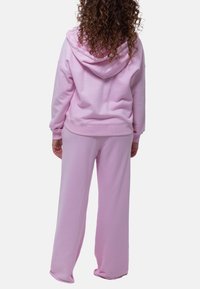 Roze hoodie en bijpassende joggingbroek, gemaakt van zachte stof met een ontspannen pasvorm, voorzien van ribgebreide manchetten en een eenvoudig ontwerp.