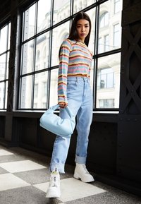 Maglietta a maniche lunghe a righe multicolori, jeans a vita alta blu, scarpe da ginnastica bianche chunky con etichette e una borsa leggera blu.