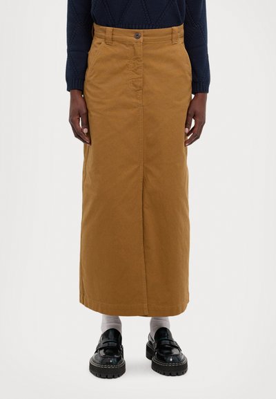Falda maxi de algodón marrón con cierre de botones en el frente, de forma recta y con aberturas laterales. Combinada con zapatos negros brillantes y calcetines grises.