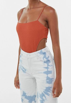 Ribbed rust-colored bodysuit with thin straps, paired with white jeans featuring a blue tie-dye pattern and a high-waisted design.