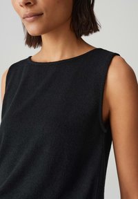 Zwarte mouwloze top met een gestructureerde stof, ronde halslijn en een losse pasvorm, die het eenvoudige ontwerp en de strakke lijnen benadrukt.