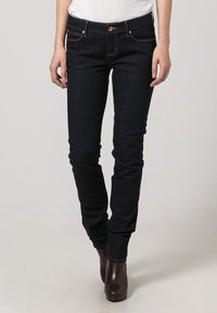 Jeans in denim blu scuro a taglio slim, con cinque tasche, dettagli in rame e cuciture sottili. Indossati con stivaletti marroni.