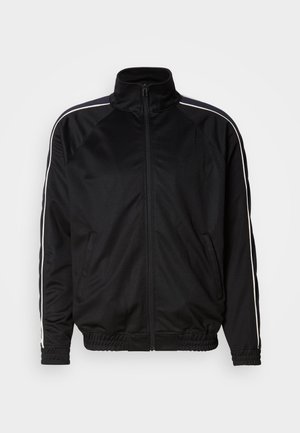 Chaqueta de chándal negra con cremallera y ribete blanco en los hombros, puños y dobladillo elásticos, y dos bolsillos frontales sobre fondo liso.