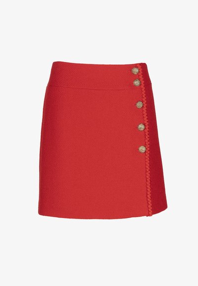 Rdeča tweed mini krilo s strukturiranim dizajnom, ki ima zlate gumbe in pleteno obrobo ob strani.