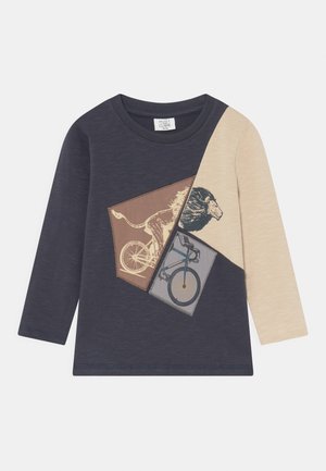 Langærmet småbørnstrøje med marineblå og beige paneler, med et billede af en løve, der cykler, på forsiden.