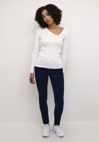 Witte lange mouwen V-hals top gecombineerd met donkerblauwe skinny jeans en witte sneakers. De top heeft een aansluitend ontwerp en een gladde textuur.
