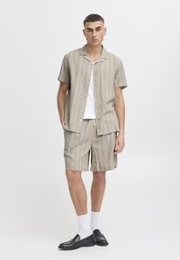Completo leggero a righe composto da camicia e pantaloncini in tonalità beige. La camicia presenta una chiusura con bottoni sul davanti e maniche corte; i pantaloncini hanno una cintura elastica.