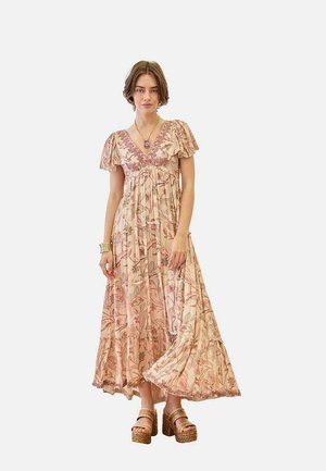 Mujer vistiendo un vestido largo y fluido con estampado floral y mangas abullonadas, de pie, combinado con sandalias de plataforma y un collar con colgante.