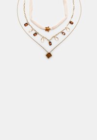 Trois colliers superposés : un choker en velours beige avec une étoile en ambre, une chaîne en or avec des perles en ambre et en goutte d'eau transparente, et une fine chaîne en or avec un pendentif en ambre.