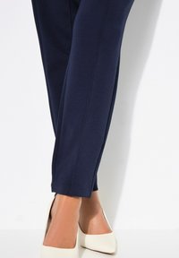 Merenkoblut stretch-housut, joissa on sileä pinta, slim fit -malli ja hienovaraiset tikkaus-yksityiskohdat, yhdistettynä kermaisiin teräväkärkisiin korkokenkiin.