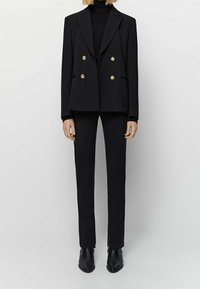 Blazer noir à double boutonnage avec des boutons dorés, associé à un pantalon ajusté assorti. Tissu lisse, design structuré et coupe slim.