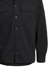 Camisa de manga larga negra hecha de tejido tejido, con dos bolsillos en el pecho, cierre de botones y detalles de costura visibles. Textura suave.