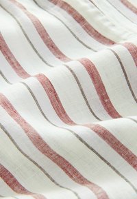 Tessuto a righe con linee alternate rosse e marroni su uno sfondo bianco; texture leggera con un evidente pattern di tessitura.