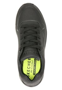 Zapato deportivo negro con detalles perforados, que presenta cordones negros, una superficie texturizada y una plantilla de espuma viscoelástica de color verde brillante.