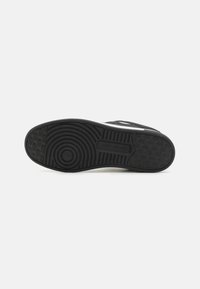Fekete gumis sneaker talp körkörös és vonalas barázdákkal. Tartalmaz egy logót és texturált részletezést az oldalán.