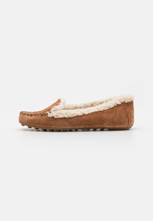 Chausson en suedine marron avec une doublure blanche duveteuse, des détails de couture mocassin et une semelle en caoutchouc texturé pour une bonne adhérence. Design plat et minimaliste.
