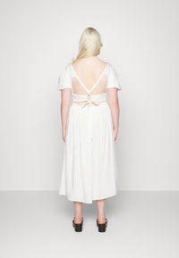 Vestido branco com mangas curtas bufantes, design de costas abertas, atado na cintura com um laço e um corte descontraído, combinado com sapatos plataforma pretos robustos.