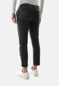 Chinos neri con una vestibilità slim, caratterizzati da una texture liscia e dettagli di cucitura minimi, abbinati a sneakers bianche.