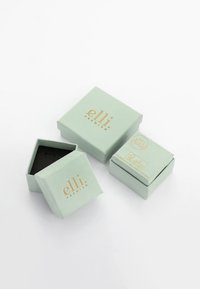 Mint zelene darilne škatle z zlatim napisom, vključno z eno odprto škatlo s črnim notranjim delom. Oblikovanje je minimalistično s kvadratnimi oblikami.