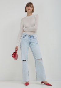 Maglietta bianca a coste con maniche lunghe, jeans azzurri strappati a gamba larga e tacchi a punta rossa. Tiene una piccola borsa rossa.