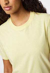 Jasnożółta bawełniana koszulka z okrągłym dekoltem, gładką fakturą, krótkimi rękawami, bez widocznych wzorów ani logo.