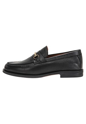 Mocasín de cuero negro con un acabado texturizado, forma alargada, acentos en tono dorado y un tacón bajo apilado.
