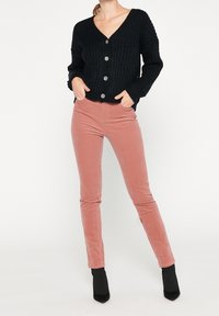 Svart ribbad cardigan med V-ringning och silverknappar, tillsammans med slim-fit, mjuka rosa corduroybyxor och svarta ribbade ankelskor.