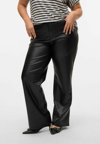 Pantaloni in finta pelle nera con design a gamba dritta, dotati di vita alta e superficie liscia. Abbinati a un top a righe e scarpe a punta.