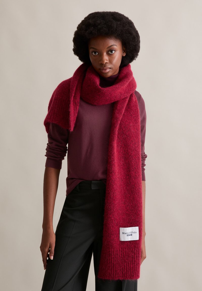 Dieprode wollen sjaal met een zachte, textuurrijke afwerking, losjes gedrapeerd. Heeft een label met "Marc O'Polo Denim" aan één uiteinde.