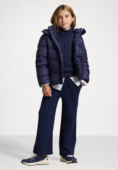 Navy puffer jacket with hood, textured knit turtleneck, and relaxed-fit navy trousers. Worn with dark athletic shoes.