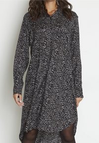 Robe noire avec un motif abstrait blanc et beige, manches longues, col et design à ourlet asymétrique, en tissu léger.