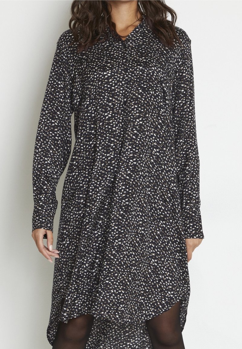 Robe noire avec un motif abstrait blanc et beige, manches longues, col et design à ourlet asymétrique, en tissu léger.