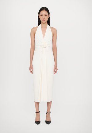 Vestido de cuello halter en tejido crema, con escote en V profundo, cintura ceñida, detalle de rosa y silueta fluida que llega a media pantorrilla.