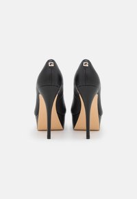 Czarne skórzane buty na wysokim obcasie z ostro zakończonym noskiem, charakteryzujące się eleganckim designem i złotym logo z tyłu.