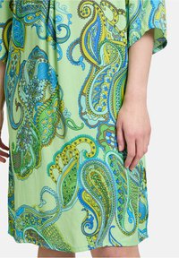 Korte mouwen jurk van lichtgroene stof met een levendig paisleypatroon in blauw en geel, voorzien van complexe details en een soepele textuur.