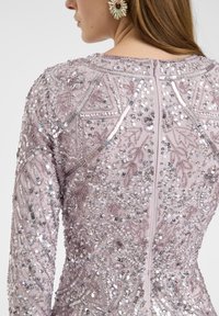 Perlenkleid in hellem Lavendel mit intricaten Paillettenmustern. Lange Ärmel, Reißverschluss auf der Rückseite und strukturierte Stoffdetails.
