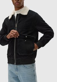 Zwarte corduroy jas met een witte nepbont kraag, voorzijde met ritssluiting en drukknopen zakken. Casual pasvorm met ribgebreide manchetten en tailleband.