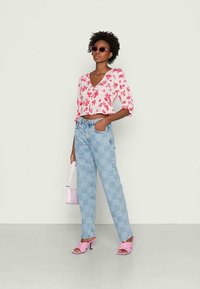 Blusa cropped floral rosa, jeans de cintura alta xadrez azul claro, saltos altos rosa e uma bolsa pequena combinando. Cabelo castanho encaracolado.