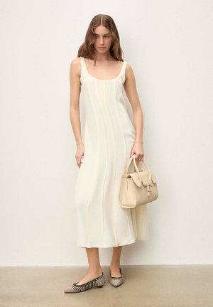 Bezruké, krémovo sfarbené šaty s vertikálnymi švami, doplnené svetlobéžovou kabelkou a čierno-béžovými vzorovanými balerínkami.