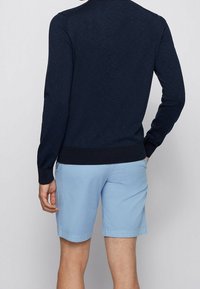Suéter de punto azul marino con mangas largas y un dobladillo acanalado, combinado con pantalones cortos azul claro de textura suave y corte recto.