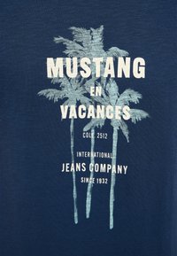Navyblaue T-Shirt mit einer Grafik von drei Palmen und weißem Text, der "Mustang en Vacances" und "International Jeans Company" angibt.