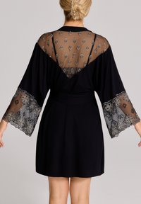 Czarna szata z przezroczystymi, haftowanymi rękawami i plecami, zdobiona kwiatowymi wzorami. Detal w postaci związania w talii, miękka tekstura i długość powyżej kolan.