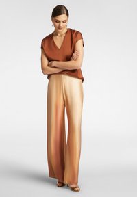 Top in satin marrone con scollo a V e maniche corte, abbinato a pantaloni ampi in satin beige e oro sfumati. Accenti dorati negli accessori.