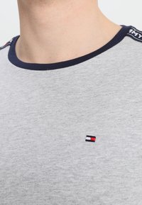 Graues Baumwoll-T-Shirt mit einem marineblauen Rundhalsausschnitt und kontrastierender Logo-Stickerei in Rot, Weiß und Blau auf der Brust.