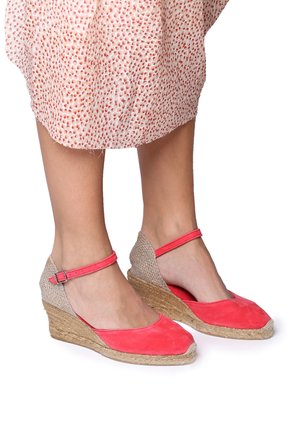 Coral suede wedge shoes with a woven jute sole and ankle strap. Features a textured interior and smooth toe area in a rounded shape.