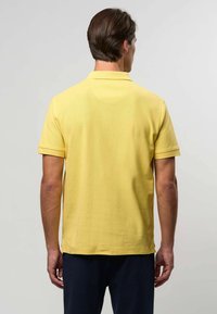 Žluté polo tričko s krátkými rukávy, texturovaná tkanina a klasický límeček. Obsahuje boční rozparky na lemu pro uvolněný střih.