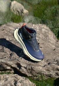 Polo vysoké turistické topánky s námornícky modrým sieťovým zvrškom, oranžovými akcentami, vystuženou špičkou a vibramovou podrážkou pre lepšiu trakciu na skalnatých povrchoch.